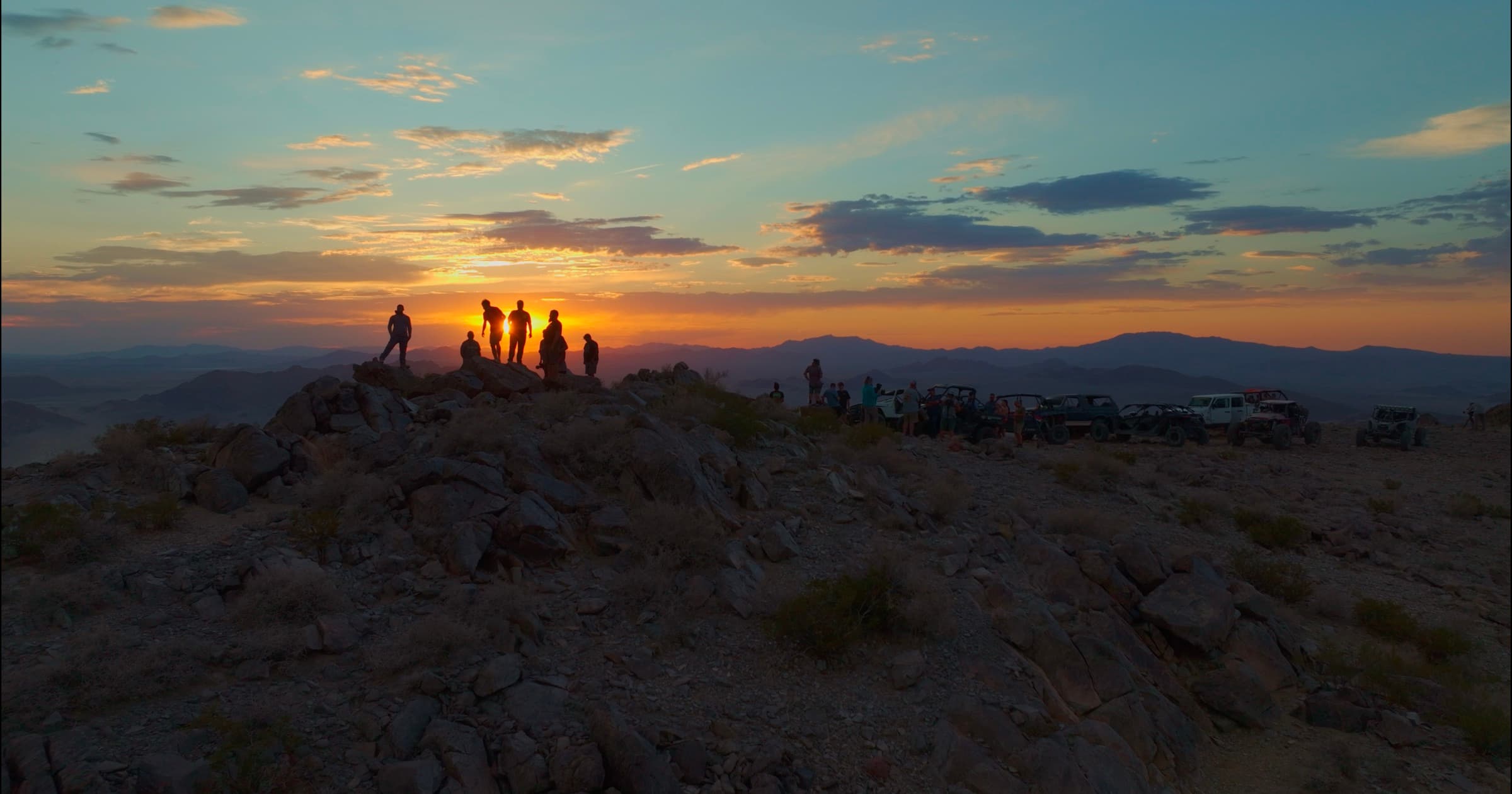 Rookie racers taking in the sunset from a desert peak, rigs lined up along the ridge